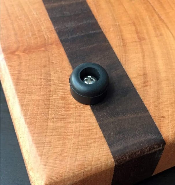 Close-up of a black rubber foot fitted to the underside of a striped cherry and walnut board