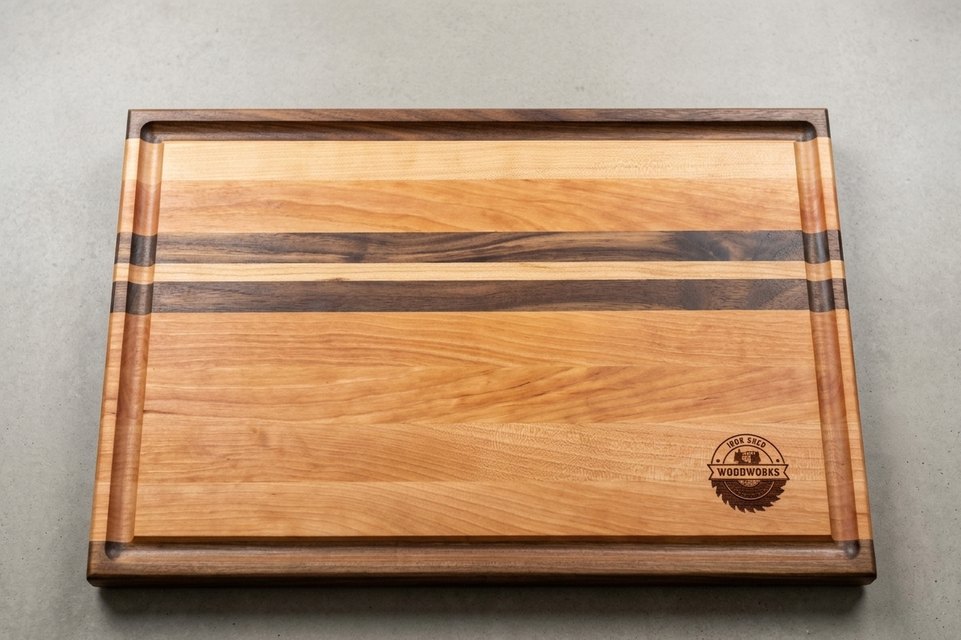 Cherry and walnut cutting board with a routed juice groove and the Iron Shed Woodworks roundel engraved in one corner