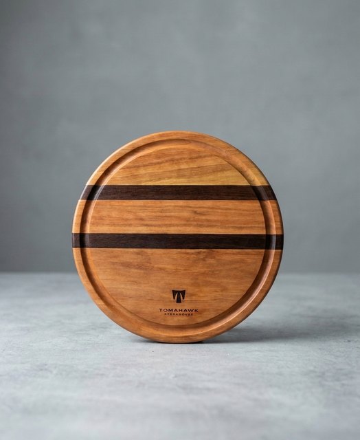 Round striped cherry and walnut serving board with a juice groove and an engraved Tomahawk logo