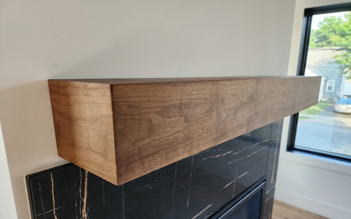 Solid walnut floating mantel spanning a black marble tile fireplace in a bright room